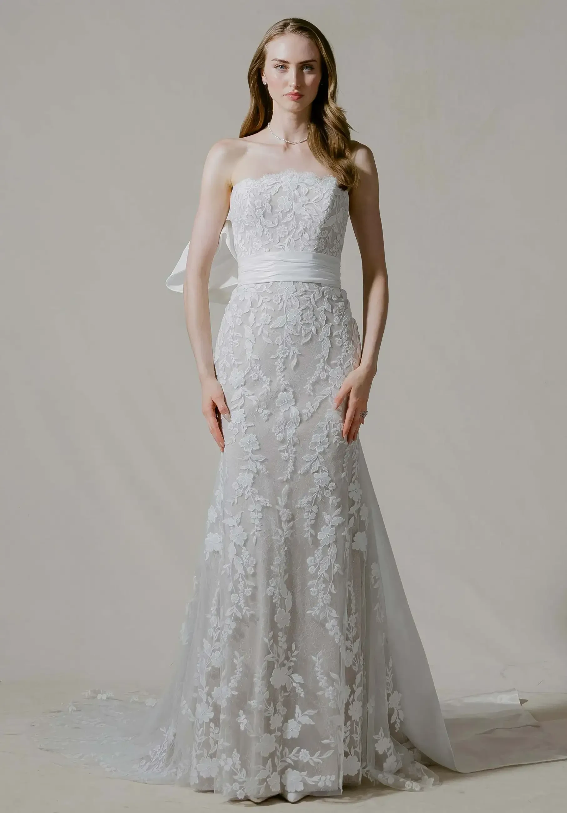 A model wearing a strapless, lace wedding gown with a fitted silhouette and a flowing train.
