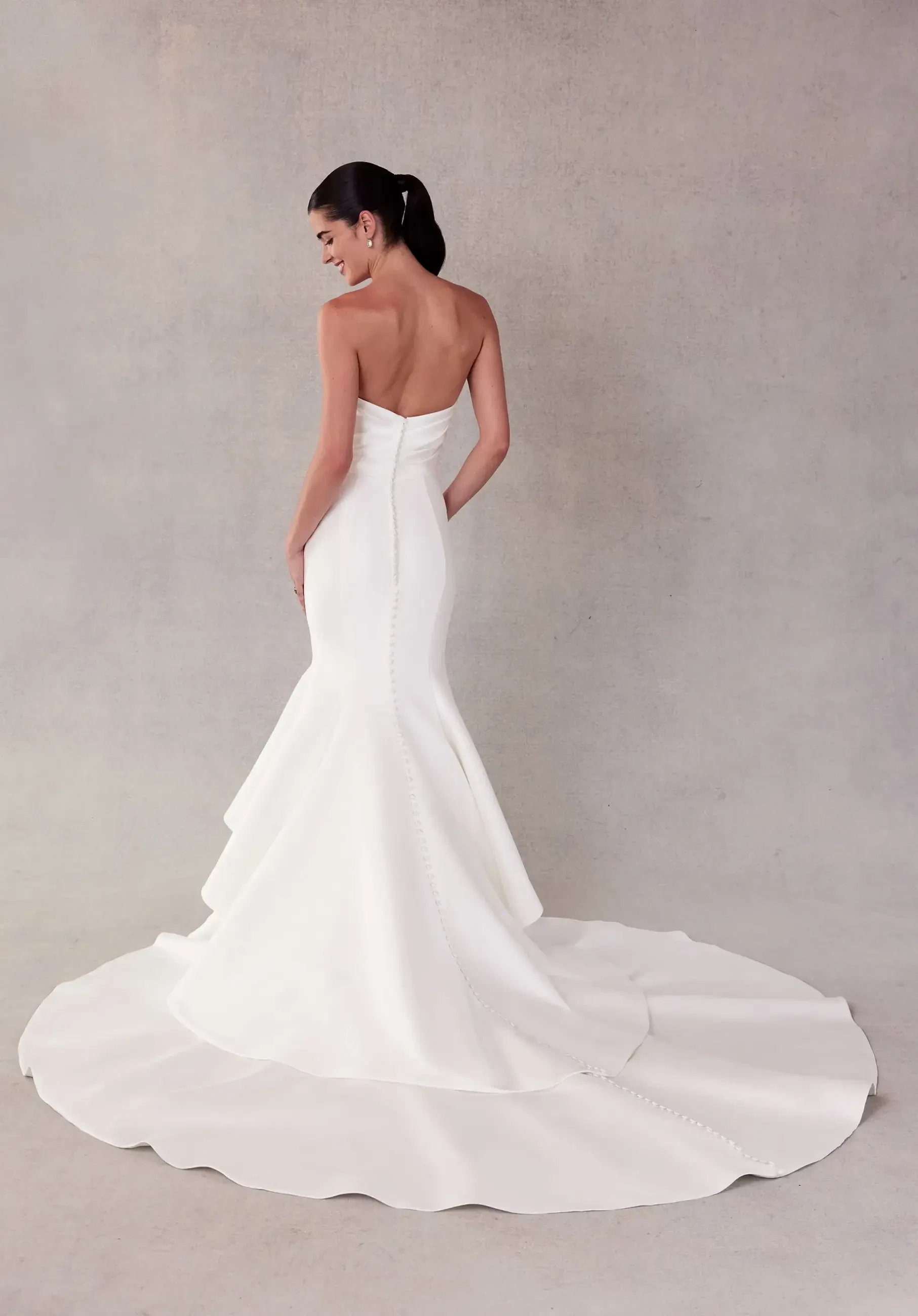 Model is wearing a mermaid wedding dress with a draped bodice and satin fabric