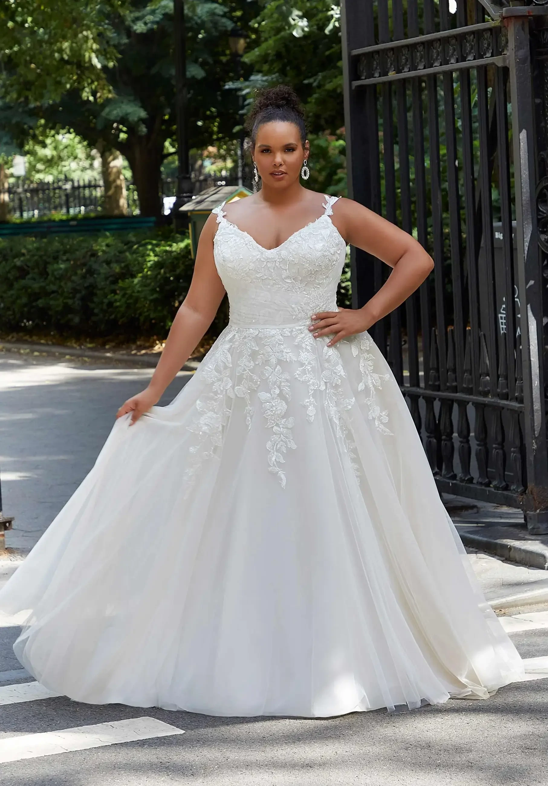 A woman wearing a white wedding dress with floral embroidery, standing gracefully outdoors.