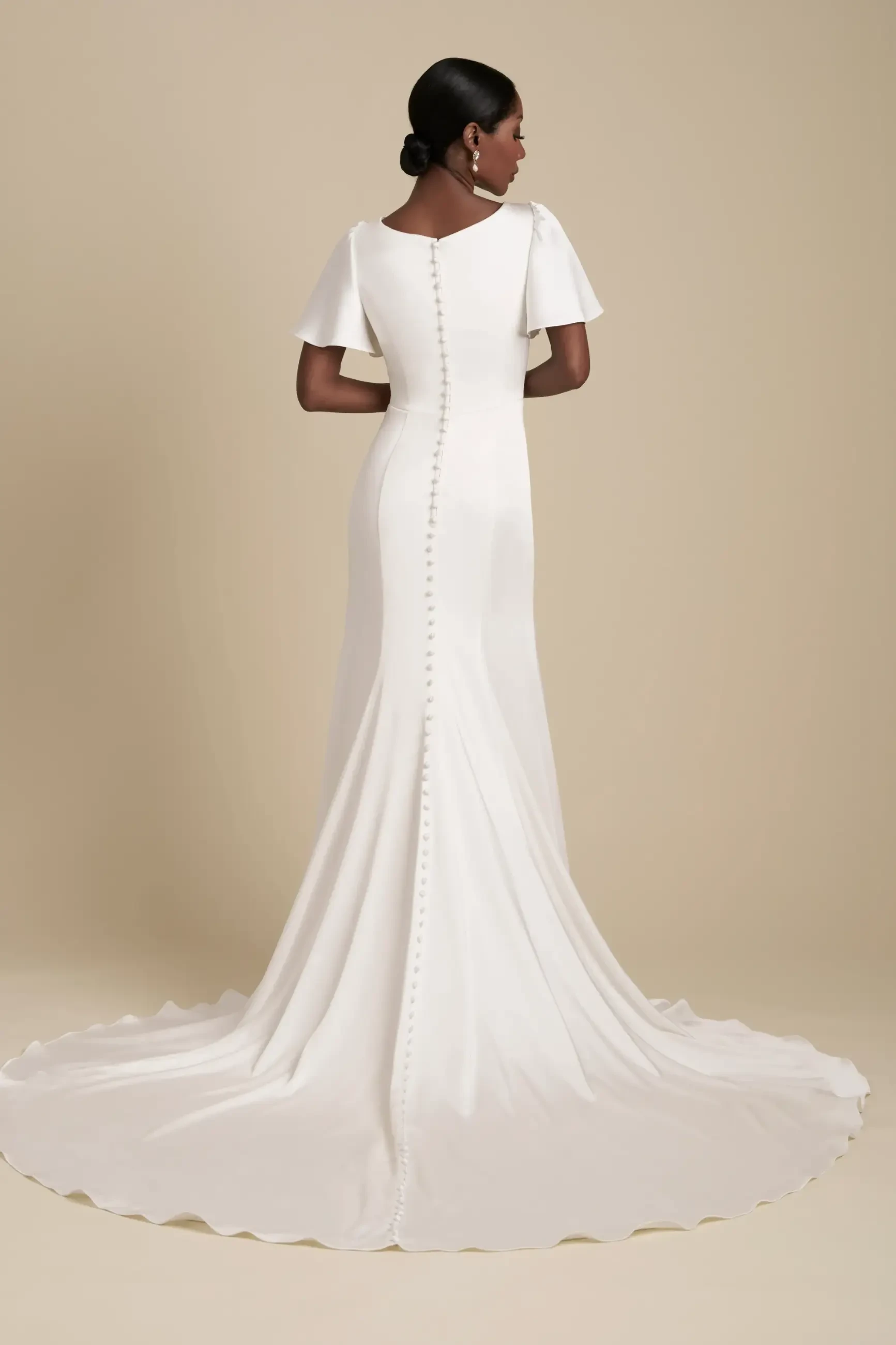 Model is wearing a modest a-line wedding dress with flutter sleeves