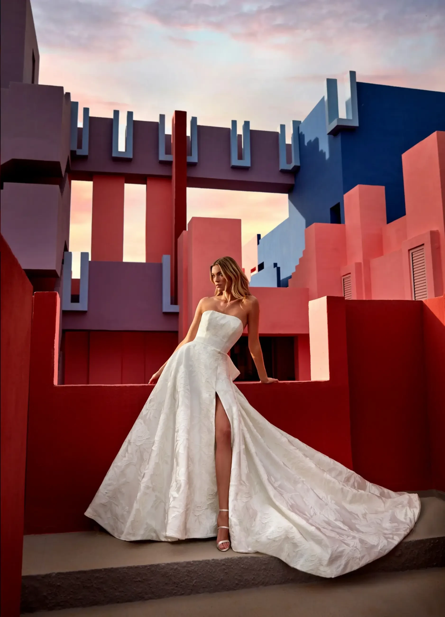 Model is wearing a floral jacquard satin ballgown with a structured silhouette and a bow detail accenting the back.