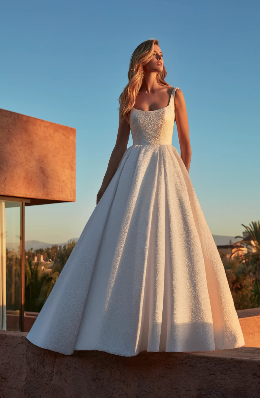 Model is wearing a ball gown wedding dress with an open back and scoop neckline