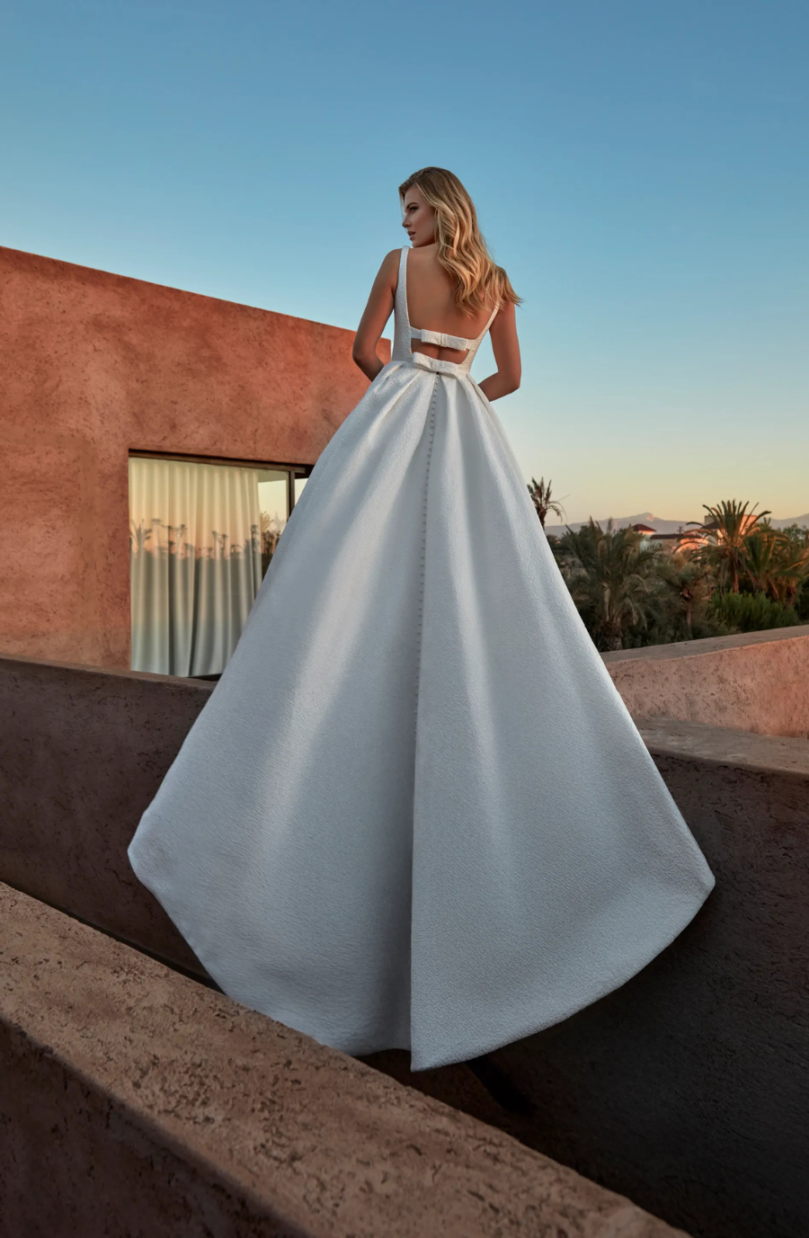 Model is wearing a ball gown wedding dress with an open back and scoop neckline