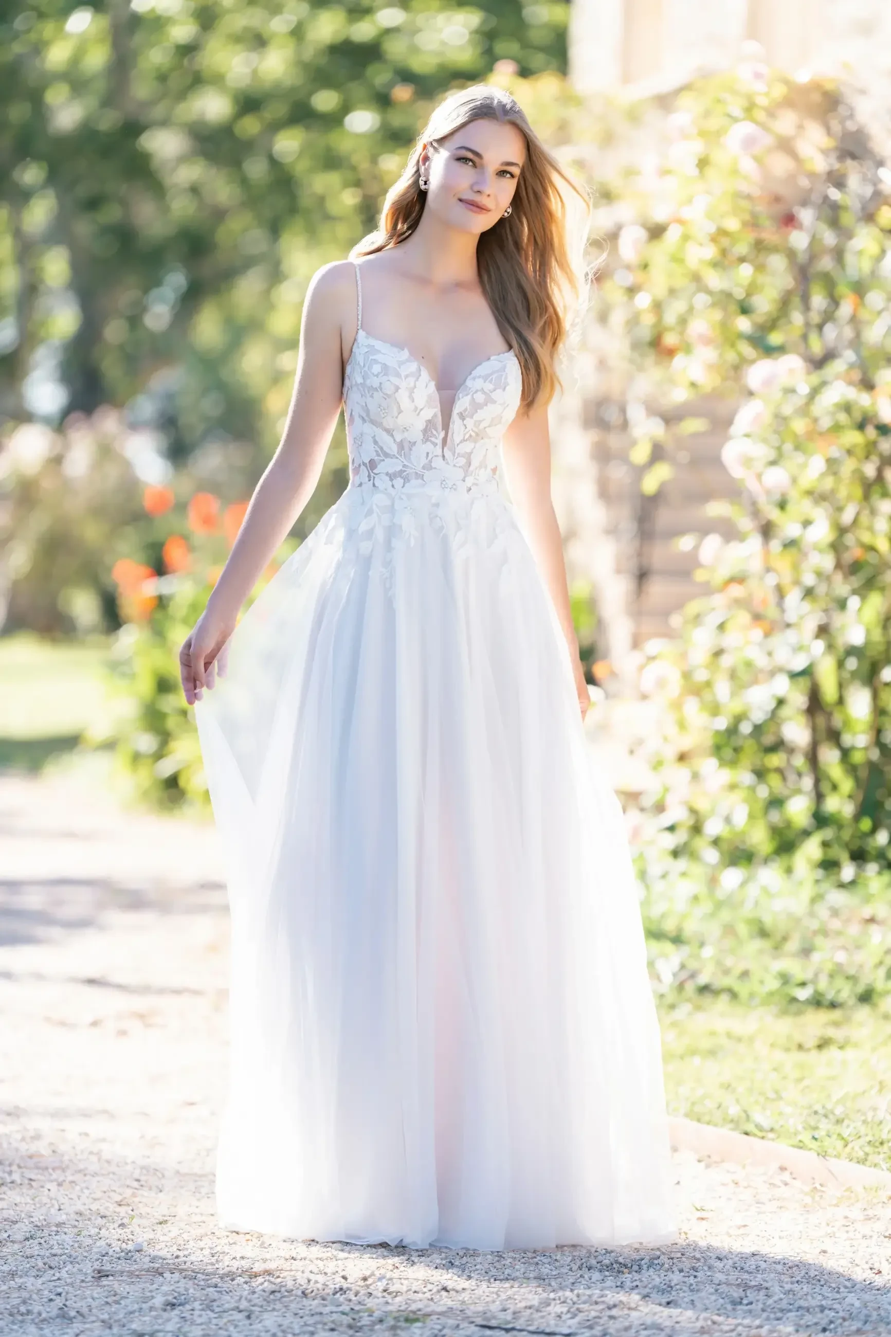 Model is wearing an A-line gown featuring dimensional beaded lace appliqués on the bodice and a layered tulle-over-crepe skirt.